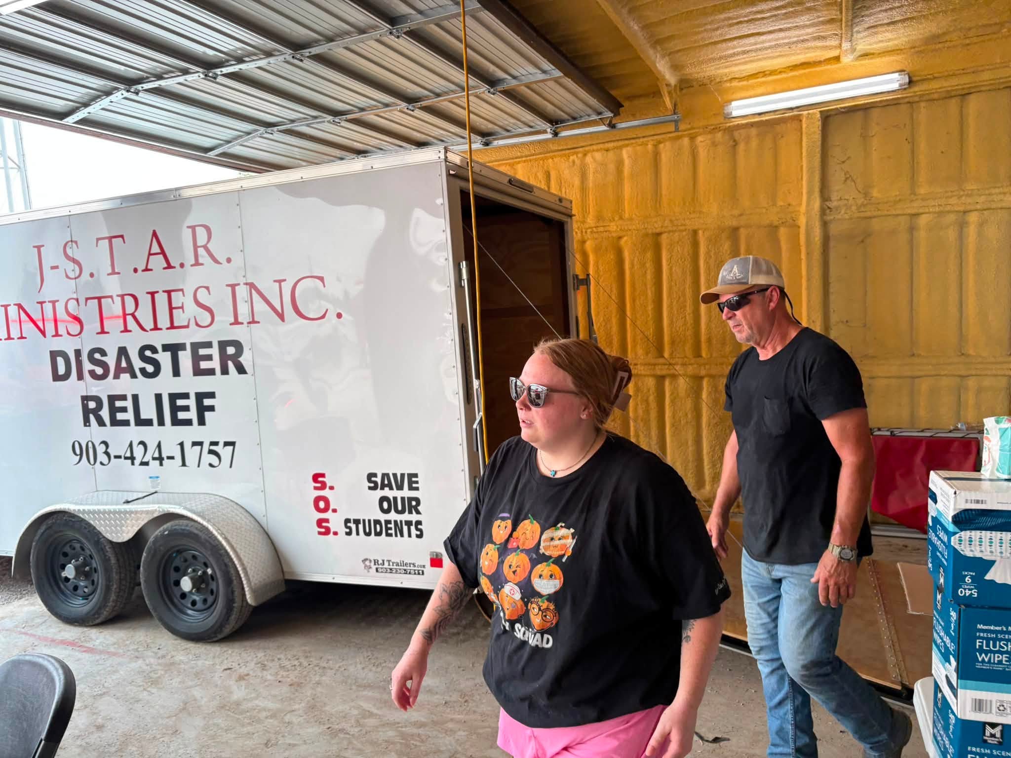 Adult helpers beside the J-STAR disaster relief trailer inside the fire station.